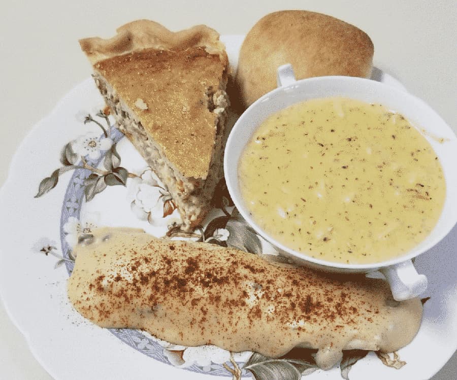 A plate featuring a slice of pie, a small roll, and a bowl of creamy soup.