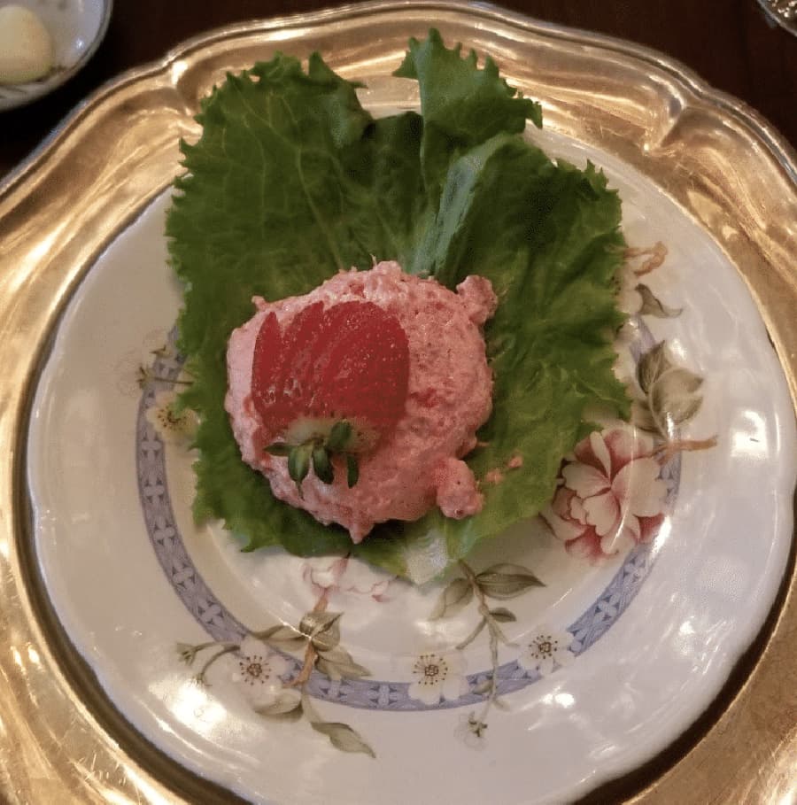 A pink strawberry mousse is served on a bed of lettuce on a decorative plate.