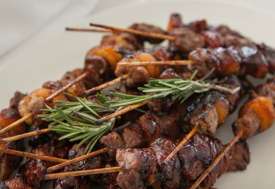 Skewers of grilled meat and shrimp garnished with fresh rosemary.
