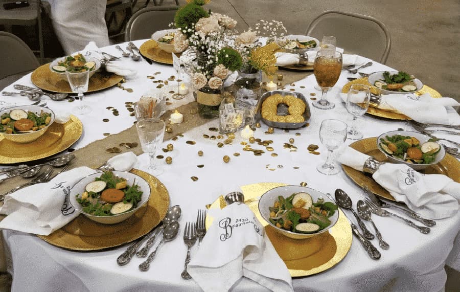 A beautifully set dining table featuring gold and white decor with bowls of salad, glassware, and decorative elements.