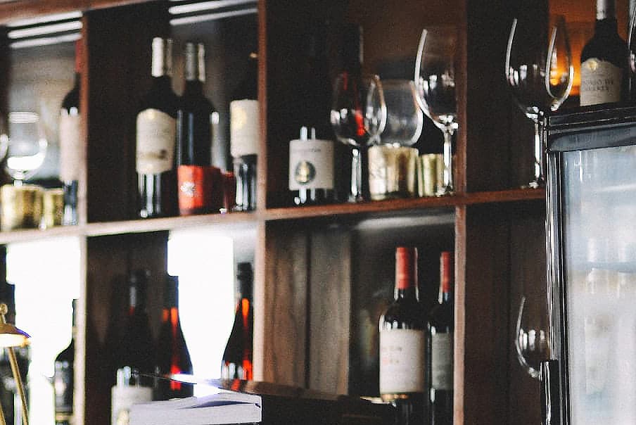 A wooden shelf displaying various bottles of wine and glassware.
