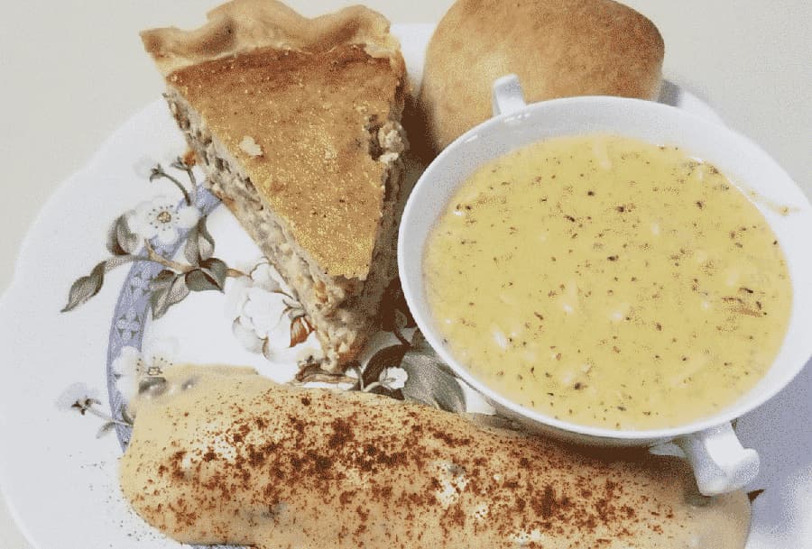 A plate with a slice of pie, a small roll, a bowl of yellow soup, and a savory pastry dusted with seasoning.