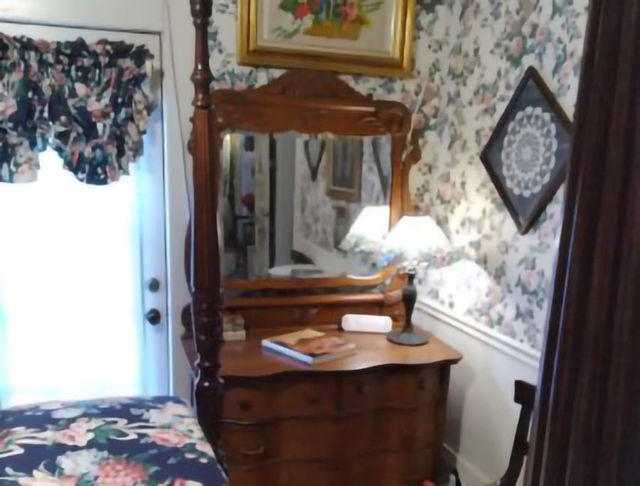 A vintage wooden dresser with a mirror and lamp in a floral wallpapered room.