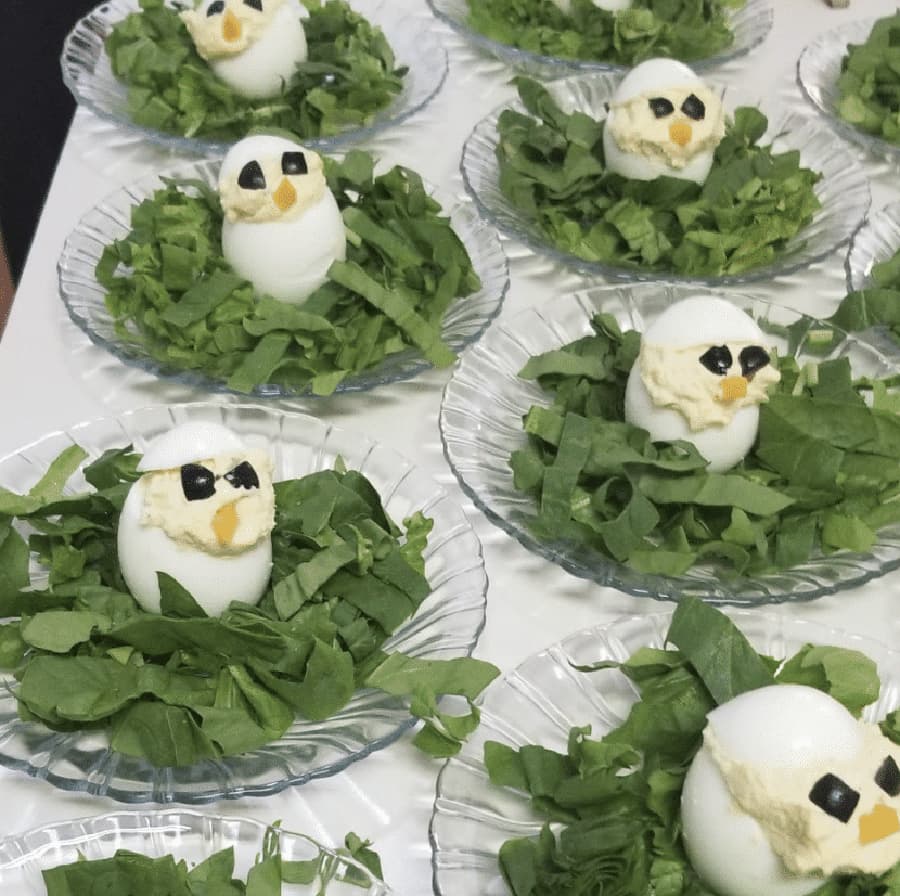 Decorative plates of hard-boiled eggs resembling ducks resting on a bed of leafy greens.