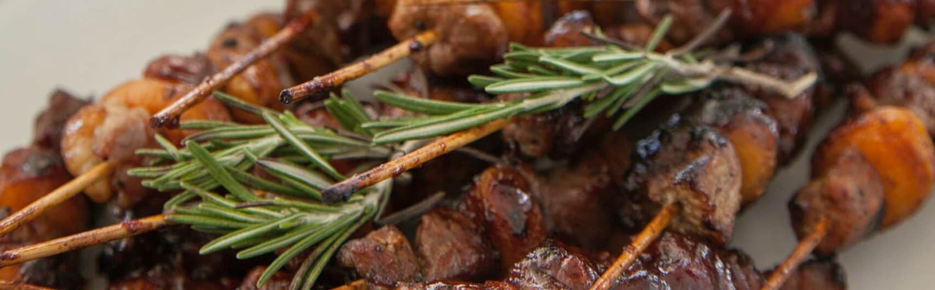 Grilled skewers of meat and shrimp garnished with fresh rosemary.
