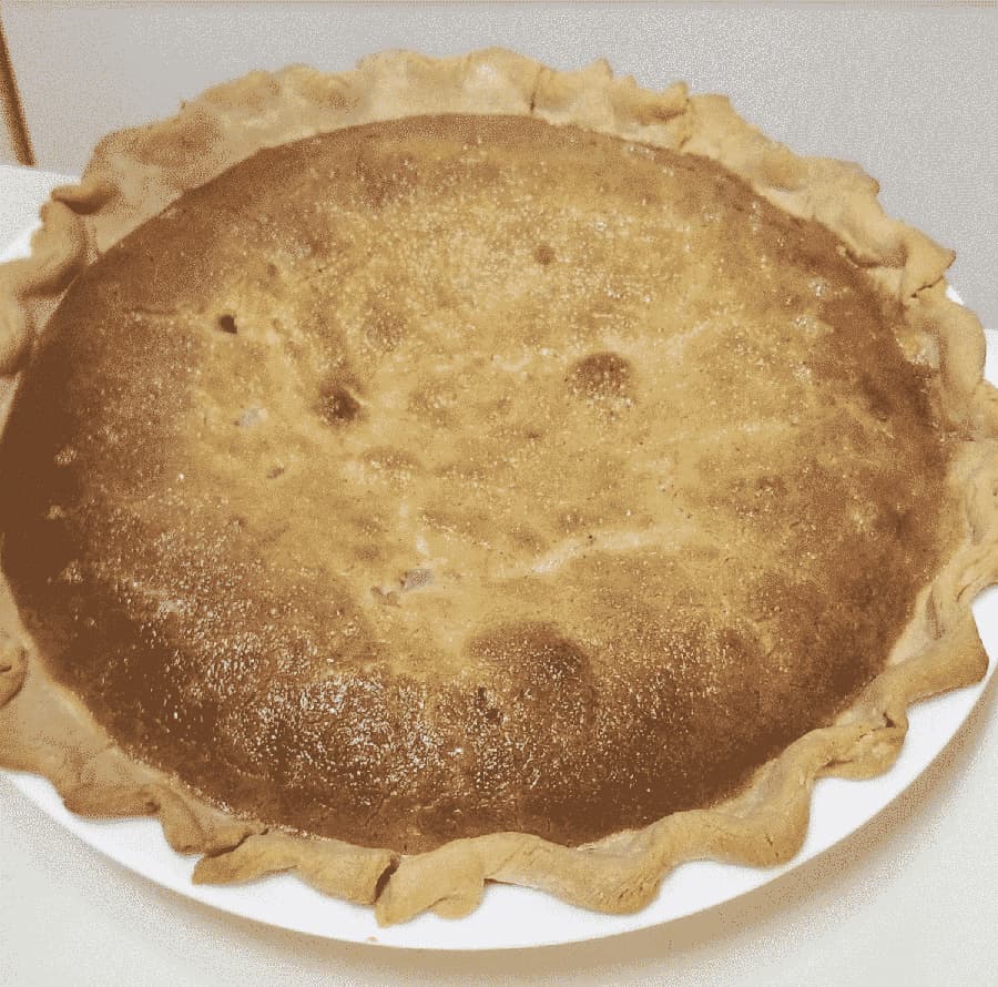 A golden-brown pie with a flaky crust sits on a white plate.