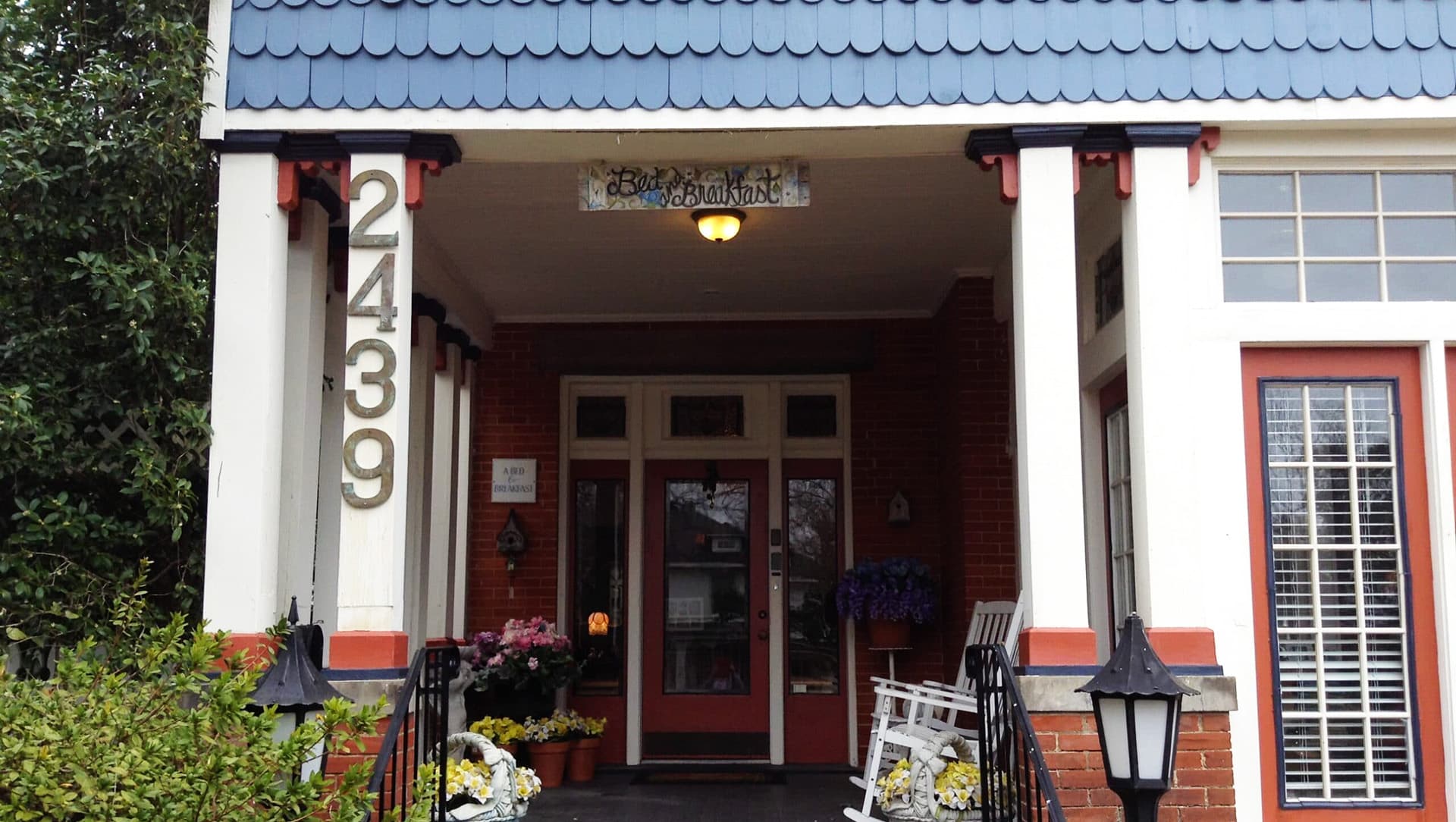 A charming entrance to a bed and breakfast with a blue roof and white columns, featuring potted flowers and a welcoming sign.